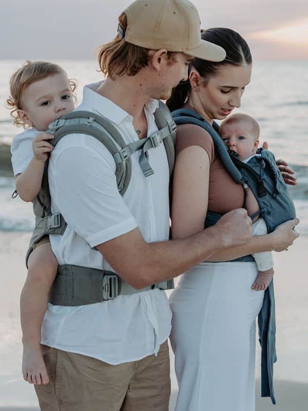 cuál es el mejor portabebés segun las necesidades de cada familia: imagen de un papa porteando con un porteo de espalda y una mama con mochila delante.